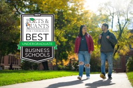 Two students walk along a path in fall alongside the Poets&Quants 2023 best business schools badge