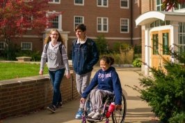Three UNH students, one in a wheelchair and two standing alongside her, walk and wheel in the courtyard at UNH's Murkland Hall.