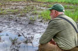 Male farmer squats before flooded field