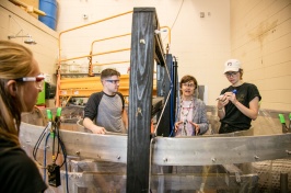 Professor and students wearing safety glasses stand behind large tank