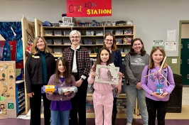 Group of four women stand behind three girls holding art projects