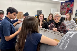 Woman in glasses laughs while standing among a group of high school students