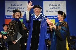 A man waves from the stage as he receives an honorary stole