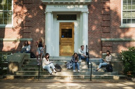 male and female students sitting on stone steps outside of brick building on campus
