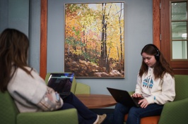 Two women students sit across from each other in chairs, working on laptops