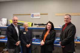 Four people stand in front of a torpedo-shaped sonar device