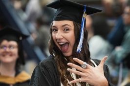 Female graduate in grad cap with huge smile shows a finger with a class ring on it