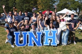 A large group of people gather behind the letters UNH at homecoming