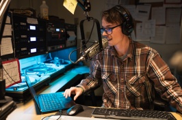 A male student wearing glasses mans the DJ booth in the WUNH studio