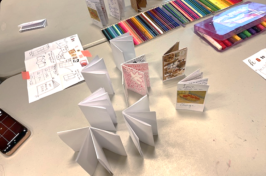 photo shows art supplies on table and done and in progress zines standing up