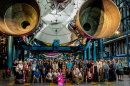 large group of scientists and students pose beneath a rocket ship