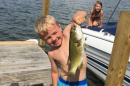a boy standing on a dock, holding up a large fish