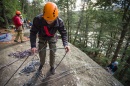 Student in orange helmet perched on edge of rock, about to rappel down