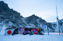 Students hold up their country's flags next to white rocket and snow-capped peaks nearby.