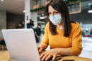 A women wearing a mask sits at a laptop