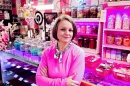 A small business owner stands in her candy shop with colorful jars and items on display behind her.