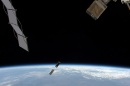 Tiny satellite floats above Earth in between much larger space science equipment.