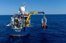 Stern of the Exploration Vessel Nautilus with a crane deploying the DriX autonomous surface vessel into the ocean.