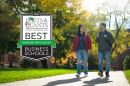 Two students walk along a path in fall alongside the Poets&Quants 2023 best business schools badge