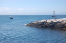 Rocky shoreline along the ocean with a boat and a sailboat in the background.