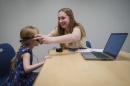 Female student puts headphones on a young girl sitting at a table