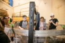 Professor and students wearing safety glasses stand behind large tank