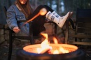 A woman wearing UNH socks roasts a marshmallow over a campfire