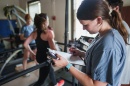 Woman student writes on a clipboard as a runner runs on a treadmill in the background