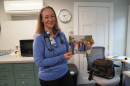 Ruth Swenson stands in a medical office holding a family portrait, wearing a stethoscope and Huggins Hospital ID badge.