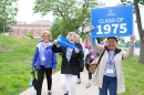A group of alumni walk in an alumni parade holding signs for the Class of 1975