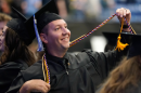 Graduate in a black robe holds up one of his cords