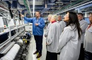 A man in a blue pullover speaks to a small group of people touring a manufacturing floor