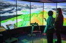 Two men, seen from behind, stand in front of a wall of computer visualization