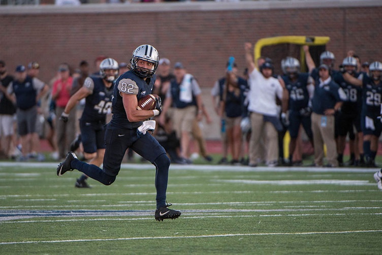 UNH football player running during the homecoming game