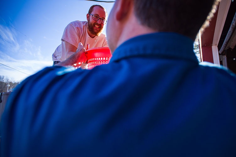 one man hands another a bucket of UNH donated tilapia