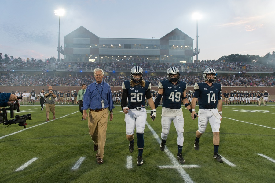 President Mark Huddleston joins three football players as they walk off the field