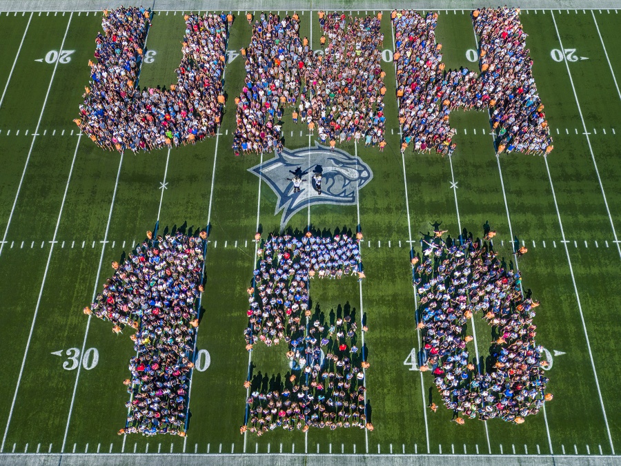 Faculty, staff and students on the football field spelling out UNH 150