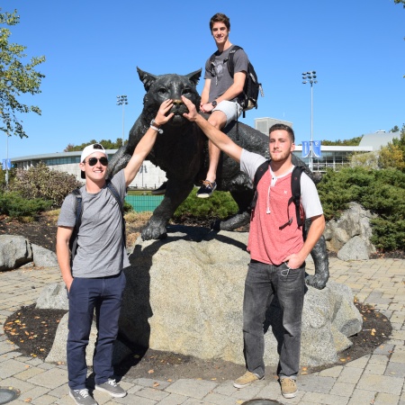 Three members of UNH's club lacrosse team pose in front of the wildcat statue 