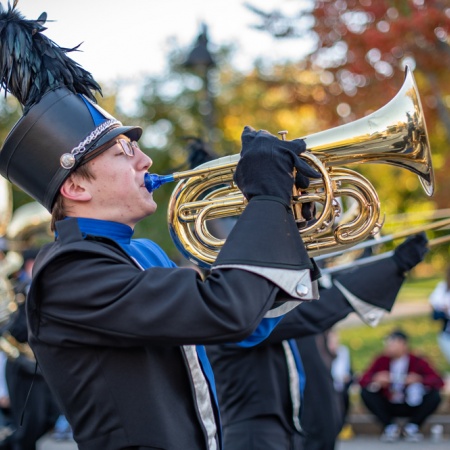 A student playing a horn in the UNH Homecoming Parade 