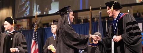 Student in Graduation Regalia shaking hands with her Dean on stage at the Honors Convocation