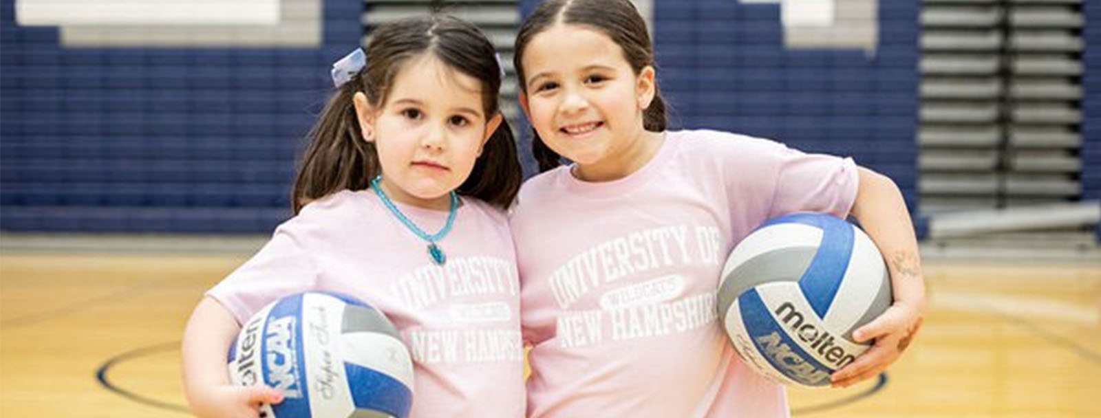 Two young girls holding volleyballs