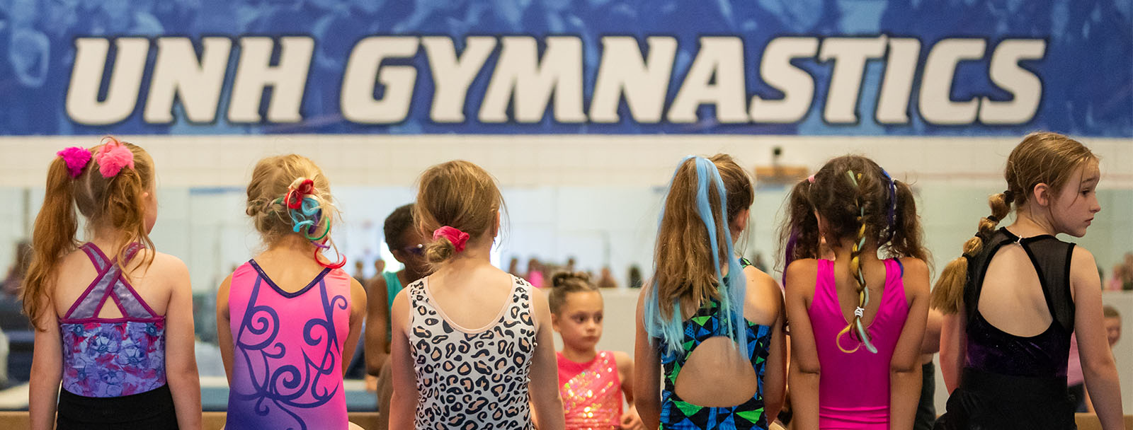 Image of students at Gymnastics Camp sitting in front of a banner that says UNH Gymnastics